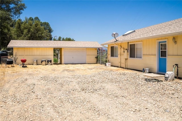 view of front of house with an attached garage, dirt driveway, and roof with shingles