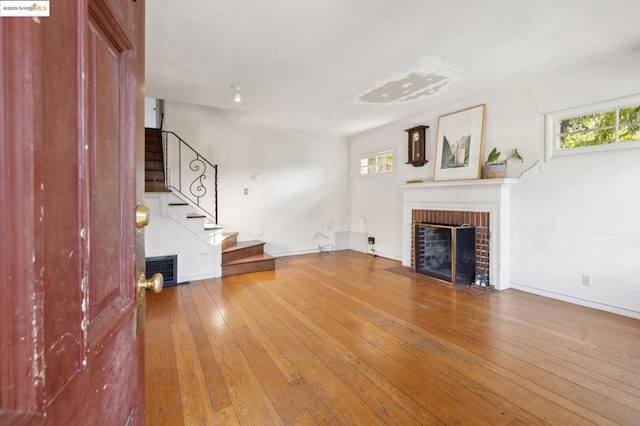 unfurnished living room featuring hardwood / wood-style flooring, a brick fireplace, and plenty of natural light