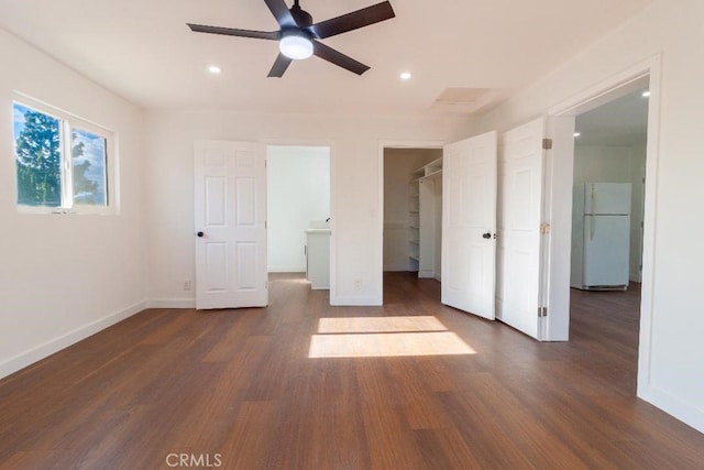 unfurnished bedroom featuring a spacious closet, dark wood-type flooring, ceiling fan, and white refrigerator