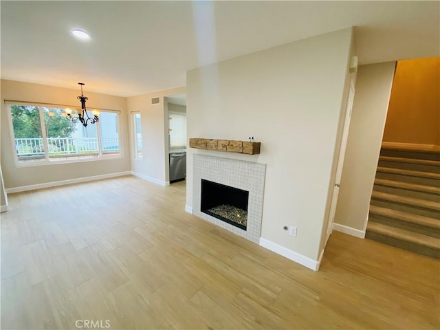 unfurnished living room with a notable chandelier, a tile fireplace, and light hardwood / wood-style floors