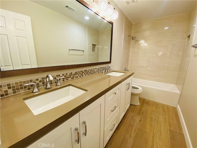 full bathroom featuring tiled shower / bath, hardwood / wood-style floors, backsplash, vanity, and toilet