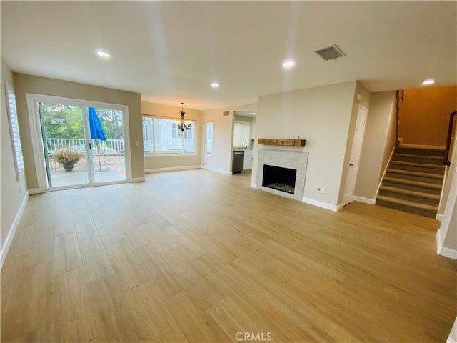 unfurnished living room featuring an inviting chandelier, a brick fireplace, and light hardwood / wood-style flooring