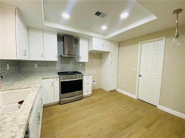 kitchen with white cabinets, hanging light fixtures, a tray ceiling, gas stove, and wall chimney exhaust hood