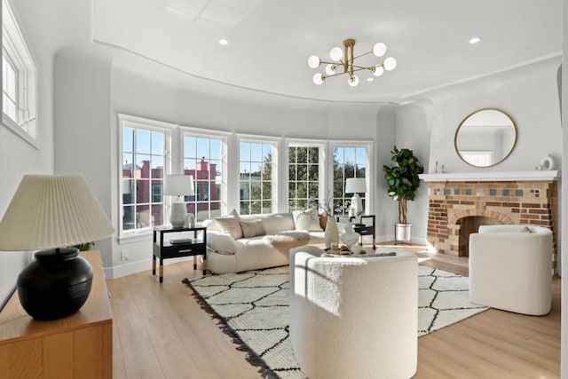 living room with ornamental molding, a brick fireplace, a notable chandelier, and light hardwood / wood-style floors