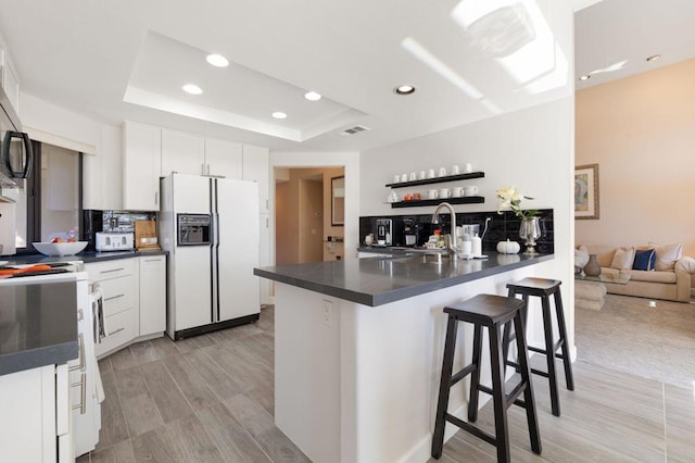 kitchen with a kitchen bar, a tray ceiling, kitchen peninsula, white appliances, and white cabinets