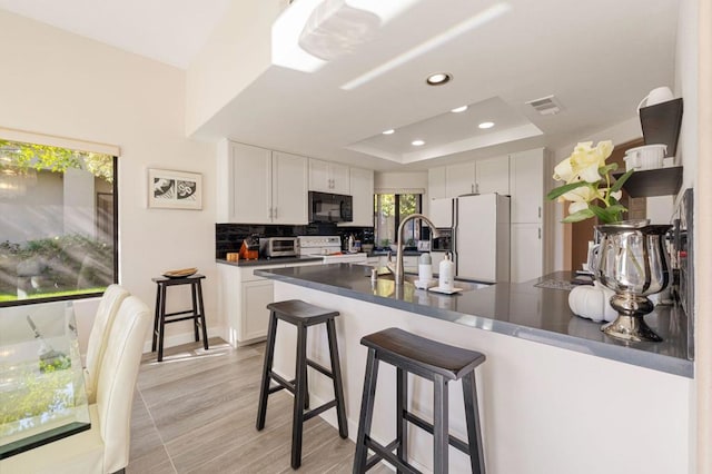 kitchen featuring tasteful backsplash, a tray ceiling, white refrigerator with ice dispenser, and white cabinets