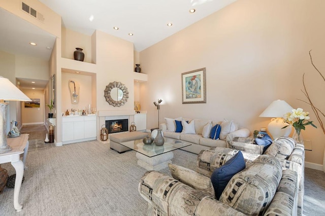 living room with a tiled fireplace, carpet floors, and a towering ceiling