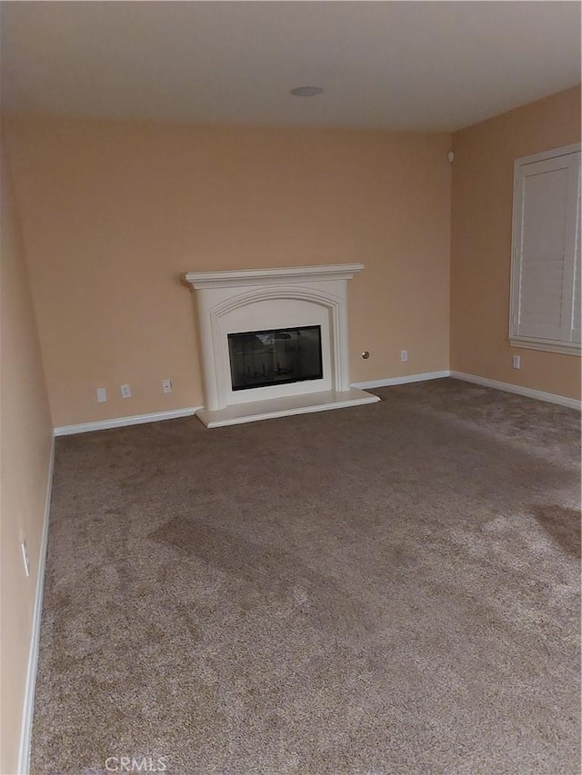 unfurnished living room with a glass covered fireplace, baseboards, and carpet