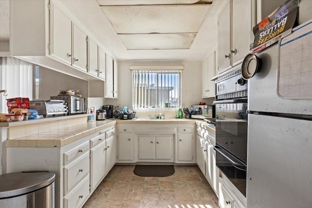 kitchen featuring tile countertops, refrigerator, sink, and white cabinets