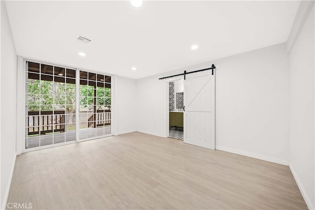 empty room with floor to ceiling windows, a barn door, and light hardwood / wood-style floors