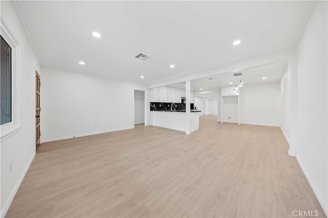 unfurnished living room featuring crown molding, sink, and light hardwood / wood-style floors