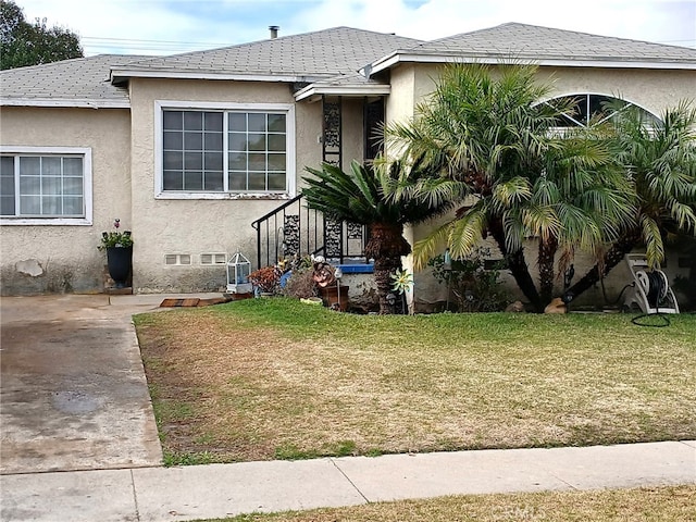 view of front of property featuring a front yard, roof with shingles, and stucco siding