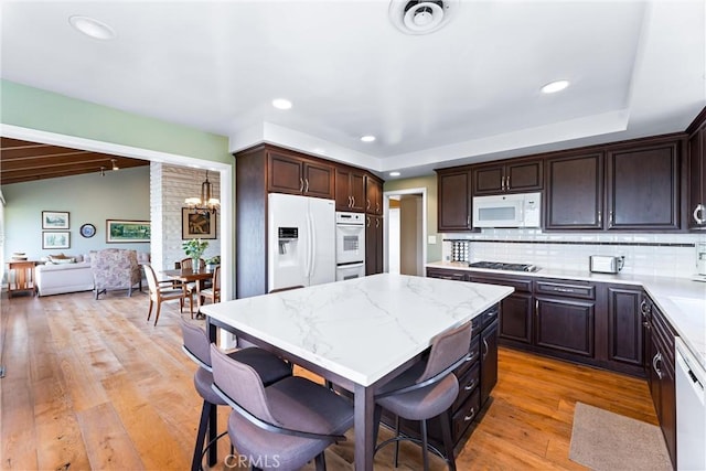 kitchen with a kitchen bar, decorative backsplash, dark brown cabinetry, white appliances, and light hardwood / wood-style flooring