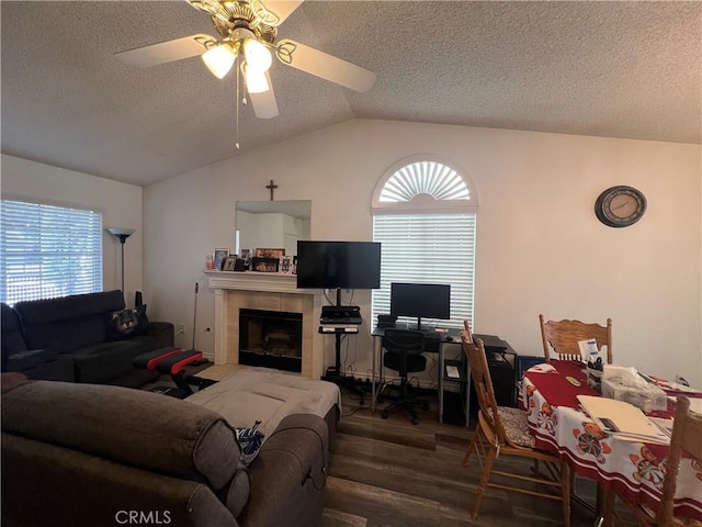 living room with vaulted ceiling, a textured ceiling, dark hardwood / wood-style floors, a tile fireplace, and ceiling fan