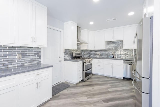 kitchen with white cabinets, stainless steel appliances, sink, and wall chimney range hood