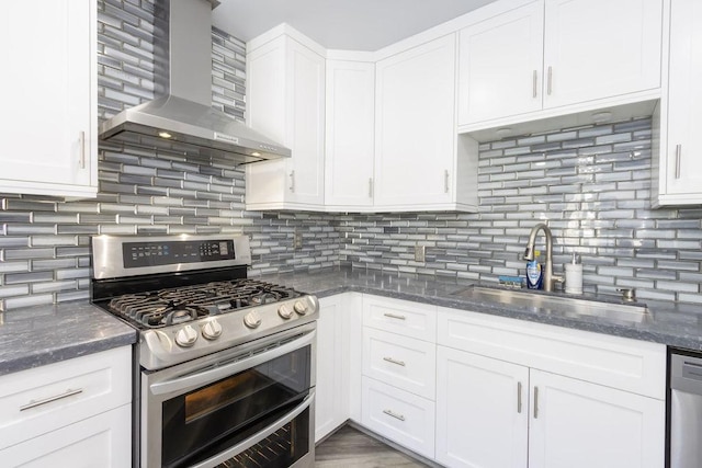 kitchen with wall chimney range hood, sink, stainless steel appliances, white cabinets, and dark stone counters