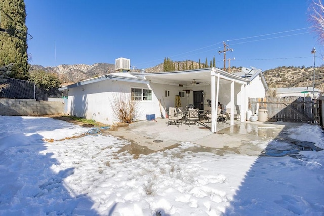 snow covered house with central AC unit, a mountain view, a patio, and ceiling fan