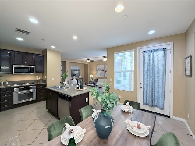 kitchen with an island with sink, sink, light tile patterned floors, light stone counters, and stainless steel appliances