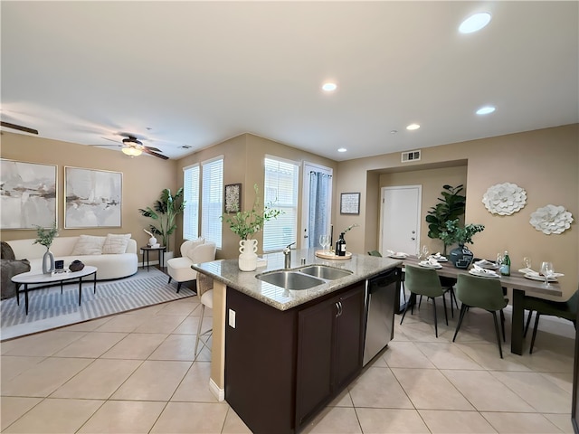 kitchen with sink, light tile patterned floors, light stone counters, an island with sink, and stainless steel dishwasher