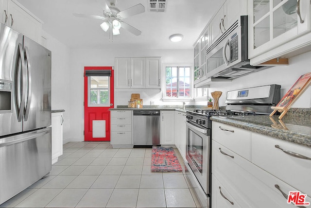 kitchen with white cabinetry, dark stone countertops, light tile patterned floors, ceiling fan, and stainless steel appliances