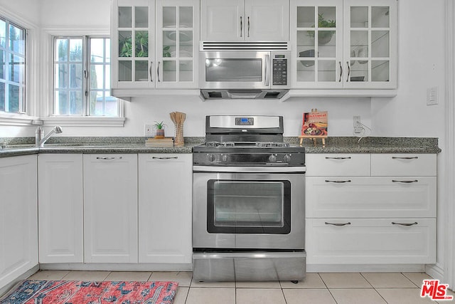 kitchen with light tile patterned floors, sink, appliances with stainless steel finishes, dark stone countertops, and white cabinets