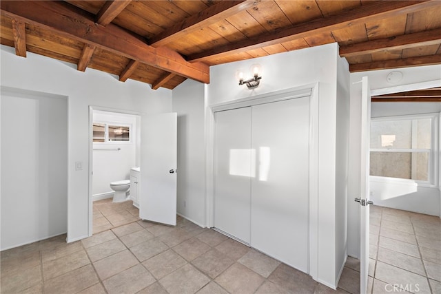 unfurnished bedroom featuring connected bathroom, lofted ceiling with beams, a closet, and wooden ceiling