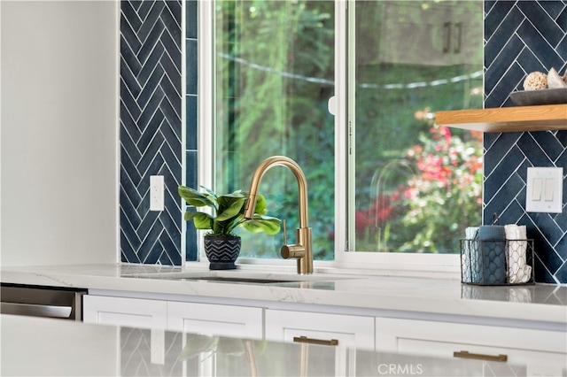 details with white cabinetry, light stone countertops, sink, and backsplash