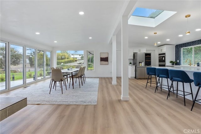 dining room with sink, vaulted ceiling with skylight, and light hardwood / wood-style floors