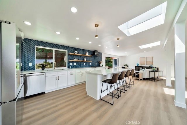 kitchen with appliances with stainless steel finishes, white cabinetry, lofted ceiling with skylight, a kitchen island, and decorative light fixtures