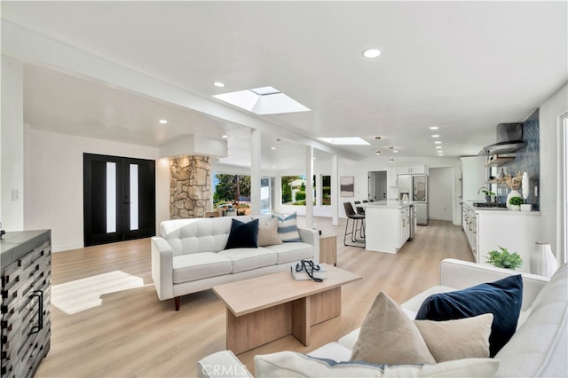 living room featuring french doors, sink, a skylight, and light hardwood / wood-style floors