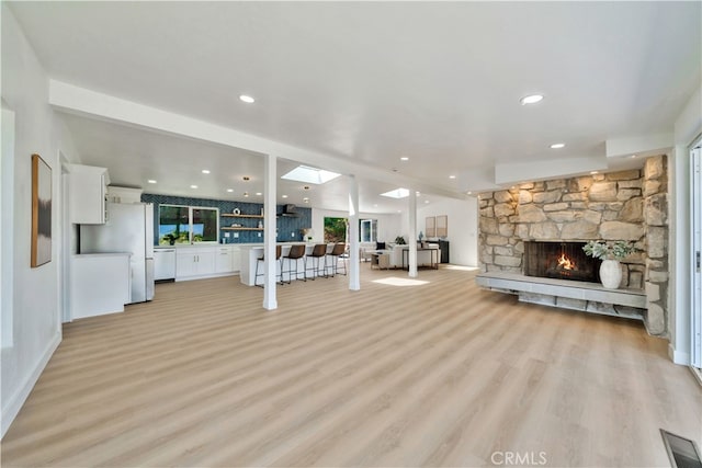 unfurnished living room with a skylight, a stone fireplace, and light hardwood / wood-style flooring