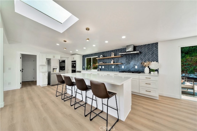 kitchen featuring white cabinetry, stainless steel fridge, a kitchen island, black gas cooktop, and wall chimney range hood