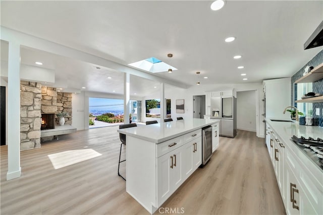 kitchen with a stone fireplace, white cabinetry, sink, stainless steel fridge, and a center island