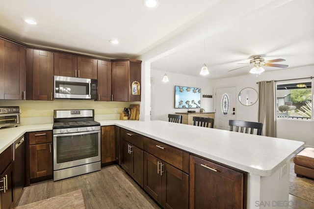 kitchen featuring a breakfast bar area, hanging light fixtures, appliances with stainless steel finishes, dark hardwood / wood-style flooring, and kitchen peninsula