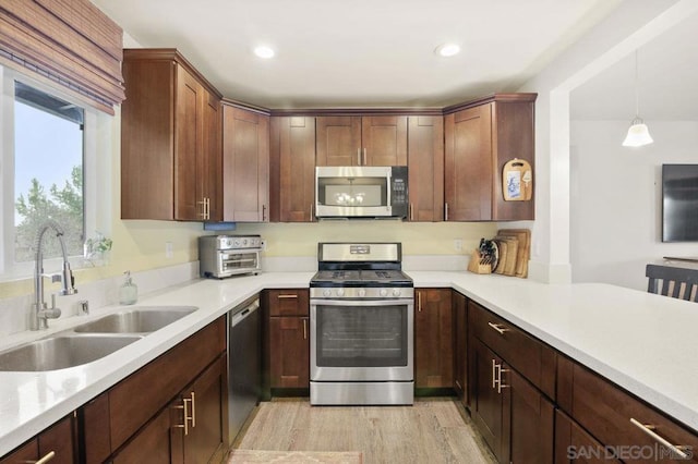 kitchen featuring pendant lighting, stainless steel appliances, light hardwood / wood-style floors, and sink