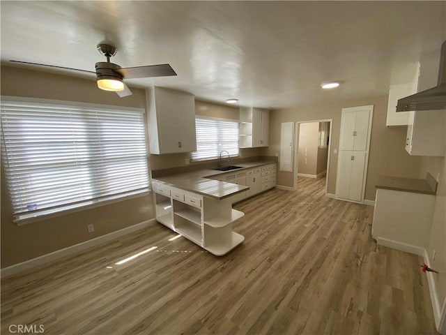 kitchen featuring sink, light hardwood / wood-style flooring, white cabinets, kitchen peninsula, and wall chimney exhaust hood