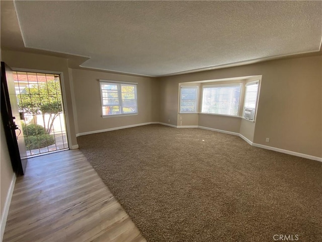 empty room with cooling unit, hardwood / wood-style floors, plenty of natural light, and a textured ceiling