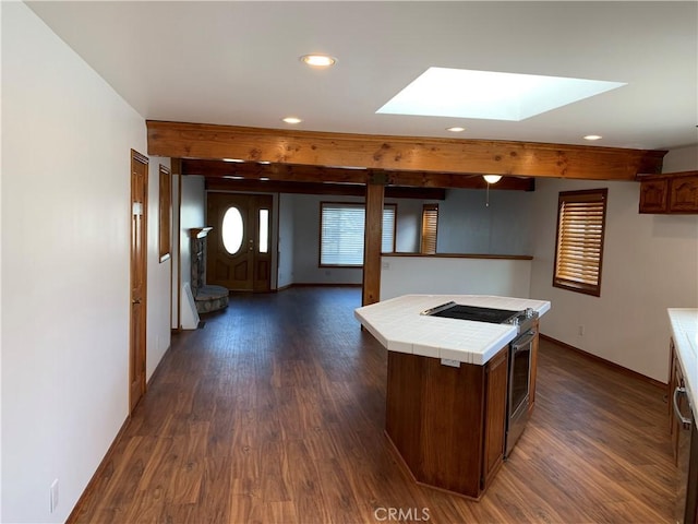 kitchen featuring a kitchen island, a skylight, tile counters, dark wood-type flooring, and stainless steel electric range