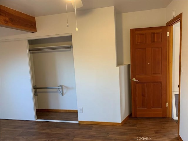 unfurnished bedroom featuring dark wood-type flooring, a closet, and beamed ceiling