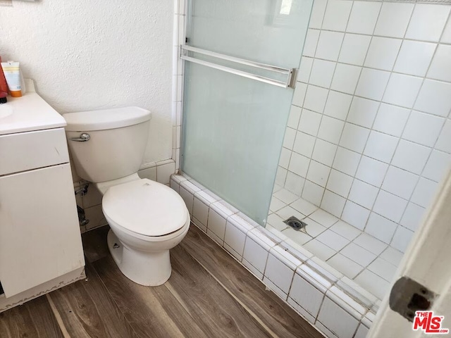 bathroom with hardwood / wood-style flooring, vanity, a shower with shower door, and toilet