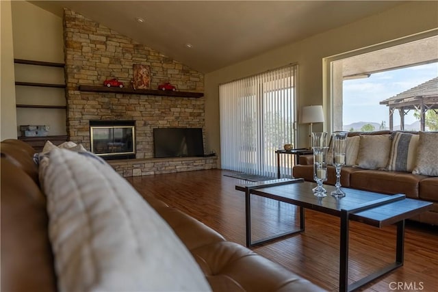 living room with vaulted ceiling, a stone fireplace, and wood finished floors