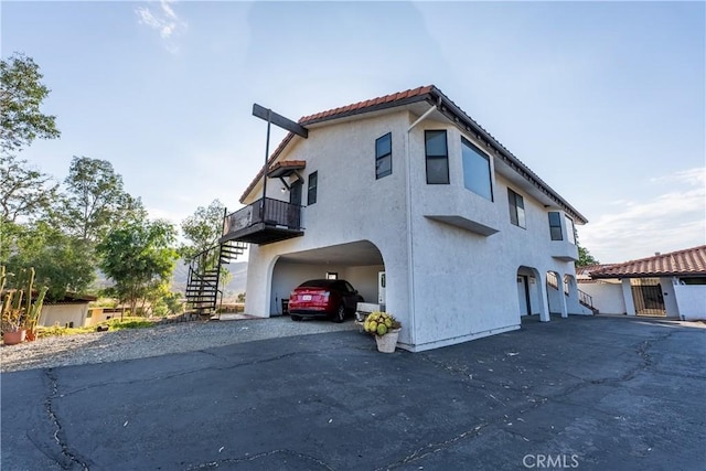 exterior space with driveway, a balcony, a tile roof, stairway, and stucco siding