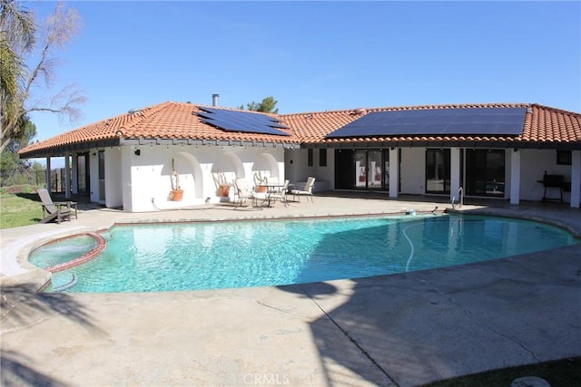 rear view of property featuring a patio, a pool with connected hot tub, solar panels, and a tiled roof