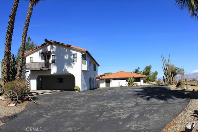 view of front of home featuring aphalt driveway, a tile roof, a balcony, and stucco siding