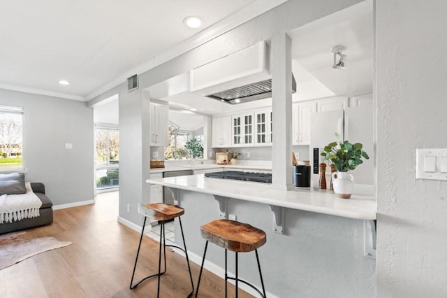 kitchen featuring appliances with stainless steel finishes, custom range hood, white cabinets, a kitchen bar, and kitchen peninsula