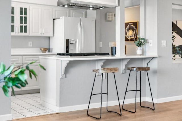 kitchen featuring white cabinetry, a breakfast bar area, white fridge with ice dispenser, kitchen peninsula, and wall chimney exhaust hood