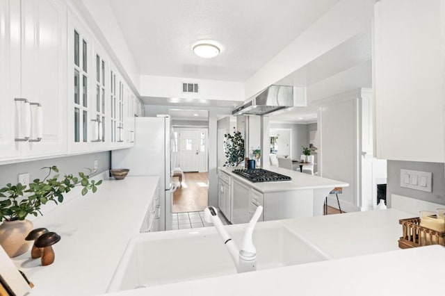 kitchen with wall chimney range hood, sink, stainless steel gas cooktop, white cabinets, and kitchen peninsula