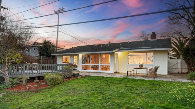 back house at dusk featuring a yard, a deck, and a patio area