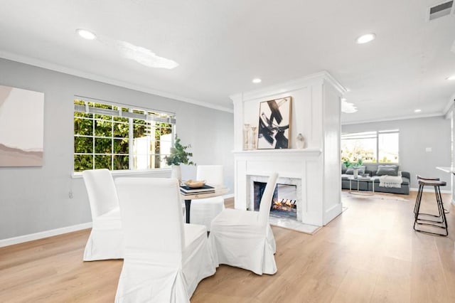 dining area with crown molding, a fireplace, and light wood-type flooring