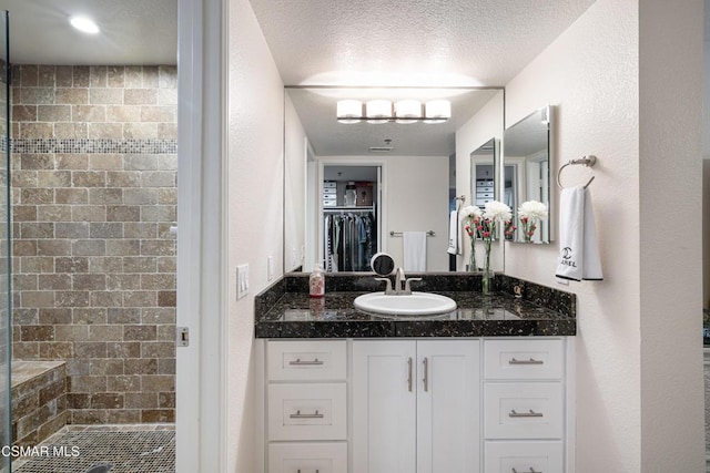 bathroom with vanity, tiled shower, and a textured ceiling